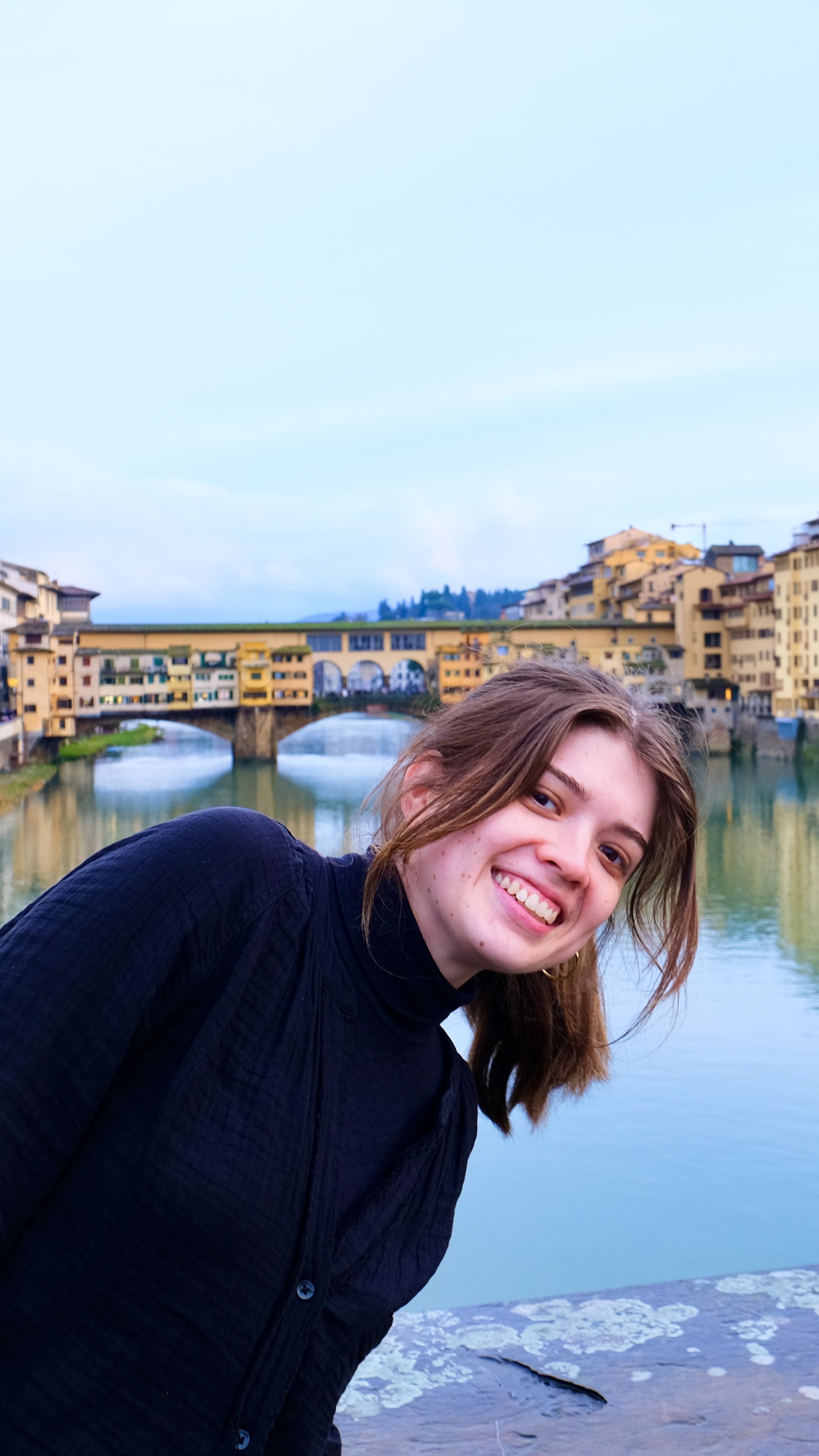 Woman smiling leaning into view with a bridge in the background.